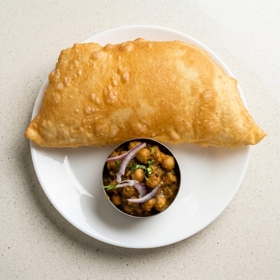 A golden-brown fried bread (puri) and a small bowl of chana masala with red onions.